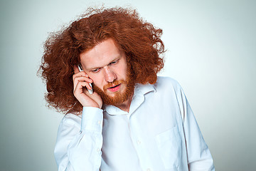 Image showing Portrait of puzzled man talking on the phone a gray background