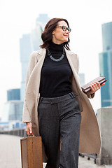 Image showing smiling middle aged brunette in a bright coat and gray trousers 