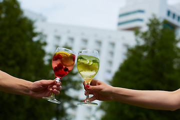 Image showing Hand holding glasses cocktail clinking together at outdoor.