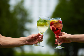 Image showing Hand holding glasses cocktail clinking together at outdoor.