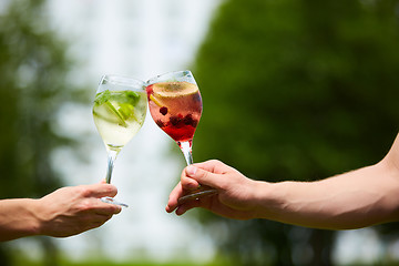 Image showing Hand holding glasses cocktail clinking together at outdoor.