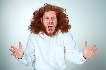 Image showing Portrait of screaming young man with long red hair and shocked facial expression on gray background