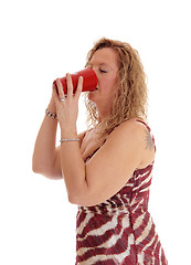 Image showing Blond woman drinking from red coffee mug.