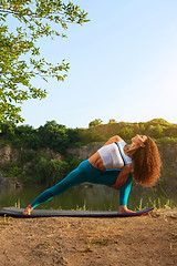 Image showing Young woman is practicing yoga near river