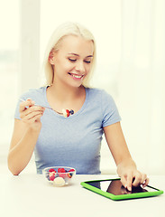 Image showing smiling woman eating fruits with tablet pc at home