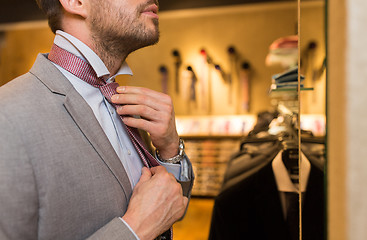 Image showing close up of man tying tie at clothing store mirror