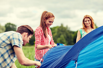 Image showing group of smiling friends setting up tent outdoors