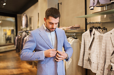 Image showing happy young man trying jacket on in clothing store