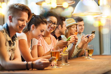 Image showing happy friends with smartphones and drinks at bar