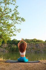 Image showing Young woman is practicing yoga near river