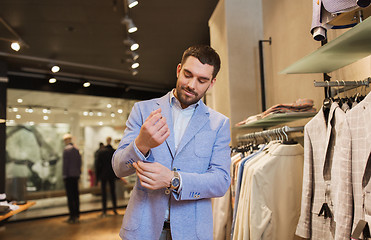 Image showing happy young man trying jacket on in clothing store