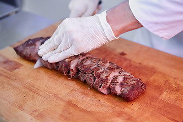 Image showing Male chef cutting big piece of beef on wooden board
