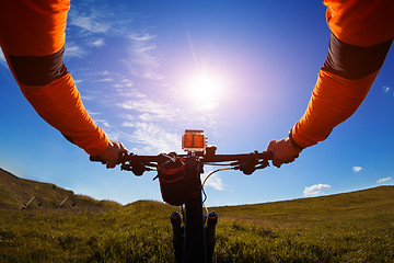 Image showing Hands in orange jacket holding handlebar of a bicycle