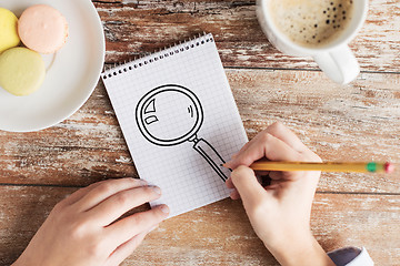 Image showing close up of hands drawing magnifier in notebook