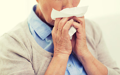 Image showing sick senior woman blowing nose to paper napkin