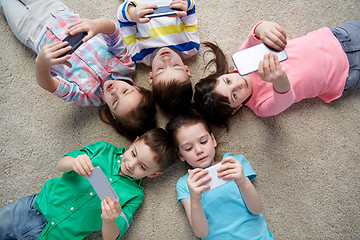 Image showing happy children with smartphones lying on floor