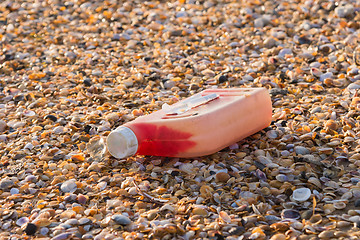 Image showing Plastic bottles of engine oil on the beach is strewn with small colorful sea shells