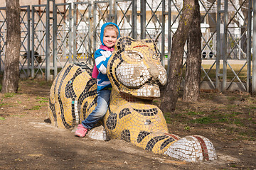 Image showing Happy girl sitting on a sculpture of a tiger on the playground in Anapa