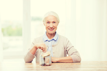 Image showing senior woman putting money into glass jar at home