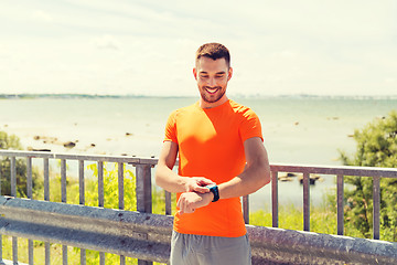 Image showing smiling young man with smart wristwatch at seaside