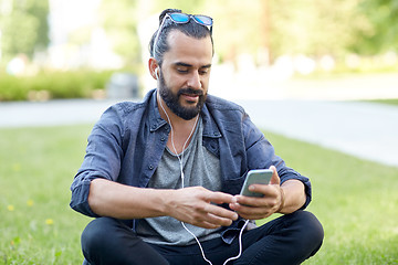 Image showing man with earphones and smartphone sitting on grass