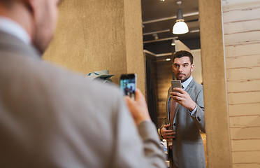 Image showing man in suit taking mirror selfie at clothing store