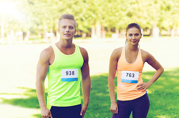 Image showing happy friends or couple with racing badge numbers