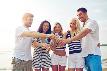 Image showing smiling friends clinking bottles on beach