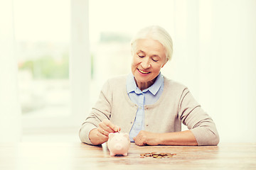 Image showing senior woman putting money to piggy bank at home