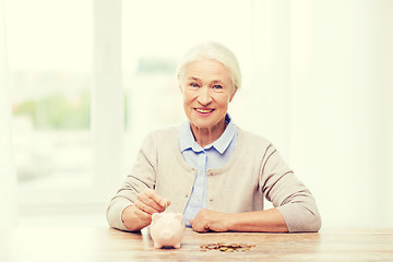 Image showing senior woman putting money to piggy bank at home