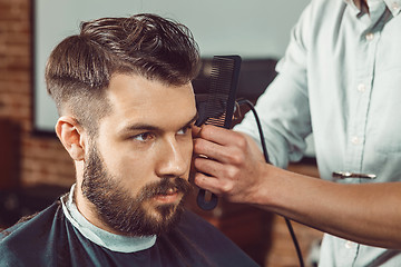 Image showing The hands of young barber making haircut to attractive man in barbershop