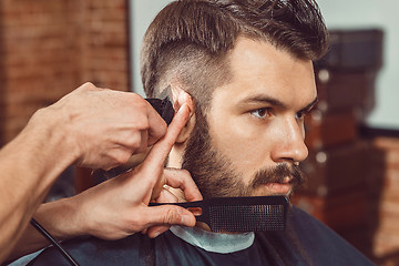 Image showing The hands of young barber making haircut to attractive man in barbershop