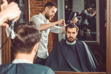 Image showing Young handsome barber making haircut of attractive man in barbershop