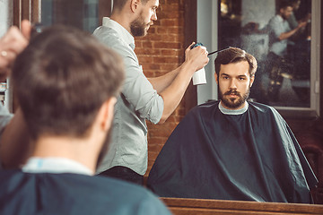 Image showing Young handsome barber making haircut of attractive man in barbershop