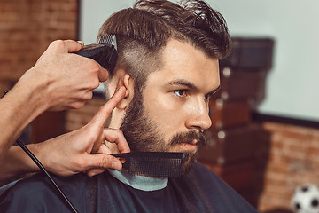 Image showing The hands of young barber making haircut to attractive man in barbershop