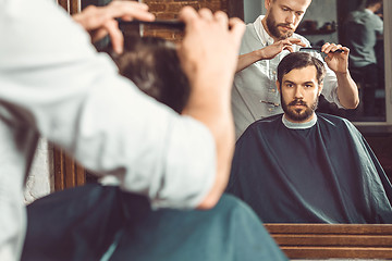 Image showing Young handsome barber making haircut of attractive man in barbershop