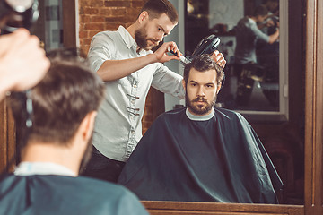 Image showing Young handsome barber making haircut of attractive man in barbershop