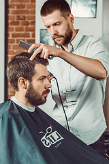 Image showing Young handsome barber making haircut of attractive man in barbershop