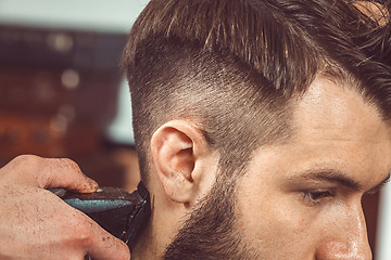 Image showing The hands of young barber making haircut to attractive man in barbershop