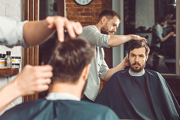 Image showing Young handsome barber making haircut of attractive man in barbershop