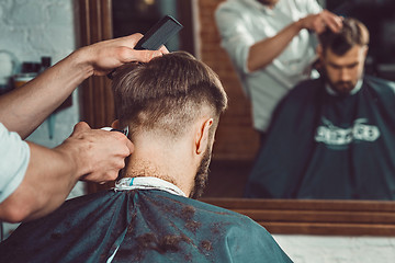 Image showing The hands of young barber making haircut to attractive man in barbershop