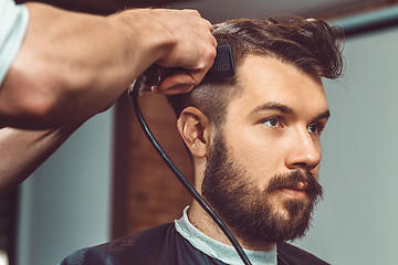 Image showing The hands of young barber making haircut to attractive man in barbershop