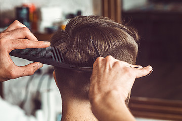 Image showing The hands of young barber making haircut to attractive man in barbershop