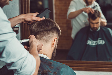 Image showing The hands of young barber making haircut to attractive man in barbershop