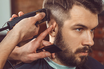 Image showing The hands of young barber making haircut to attractive man in barbershop