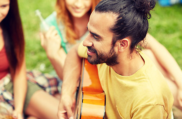 Image showing happy man with friends playing guitar at camping