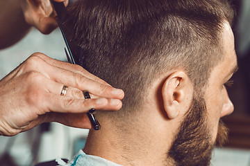 Image showing The hands of young barber making haircut to attractive man in barbershop