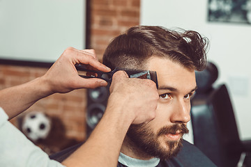 Image showing The hands of young barber making haircut to attractive man in barbershop