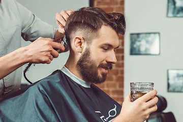 Image showing The hands of young barber making haircut to attractive man in barbershop