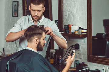 Image showing Young handsome barber making haircut of attractive man in barbershop